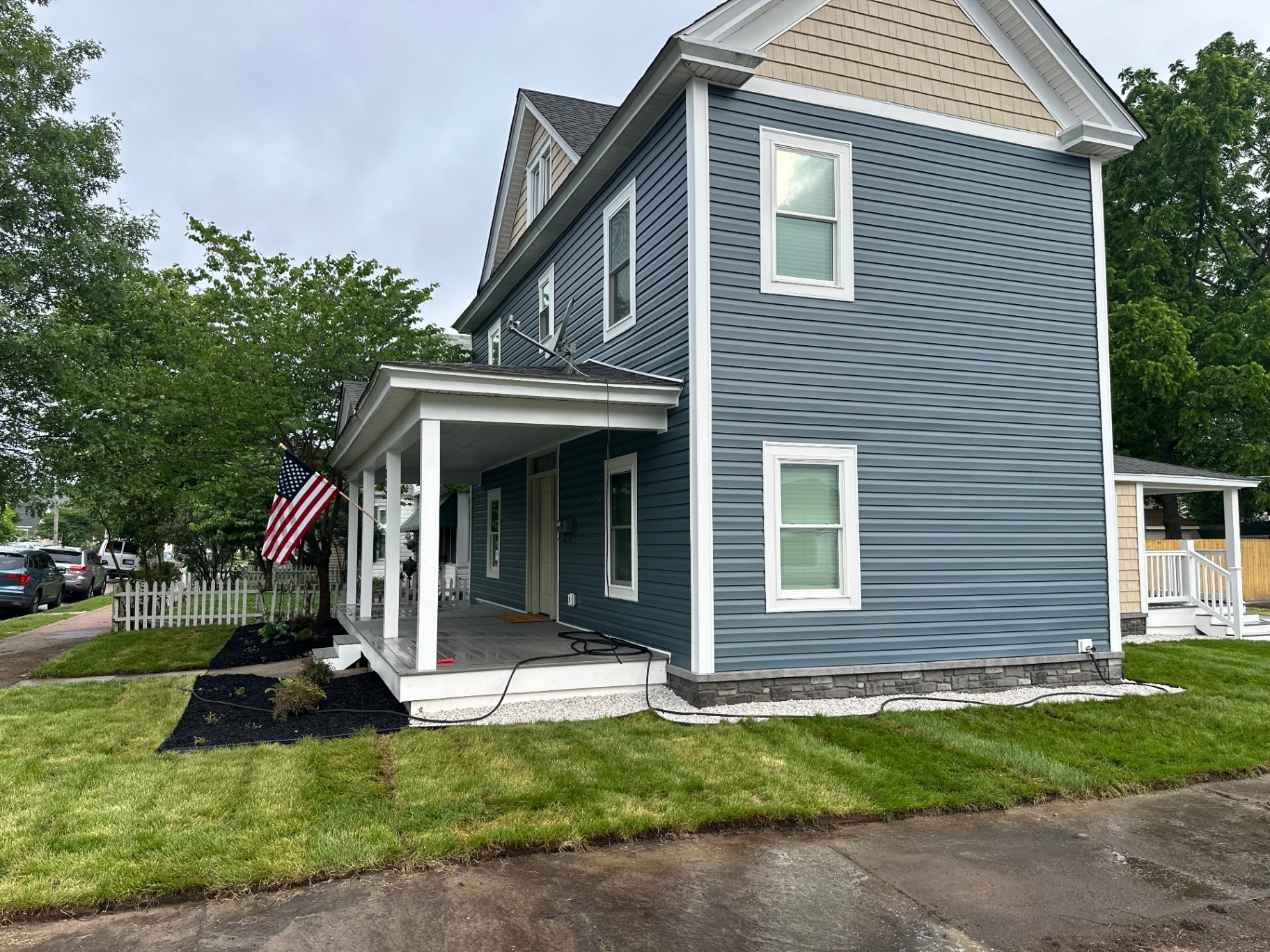 Siding installation — side view showing blue siding with white trim and stone foundation