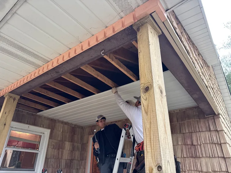 Crew fitting new soffit panels beneath the porch framing